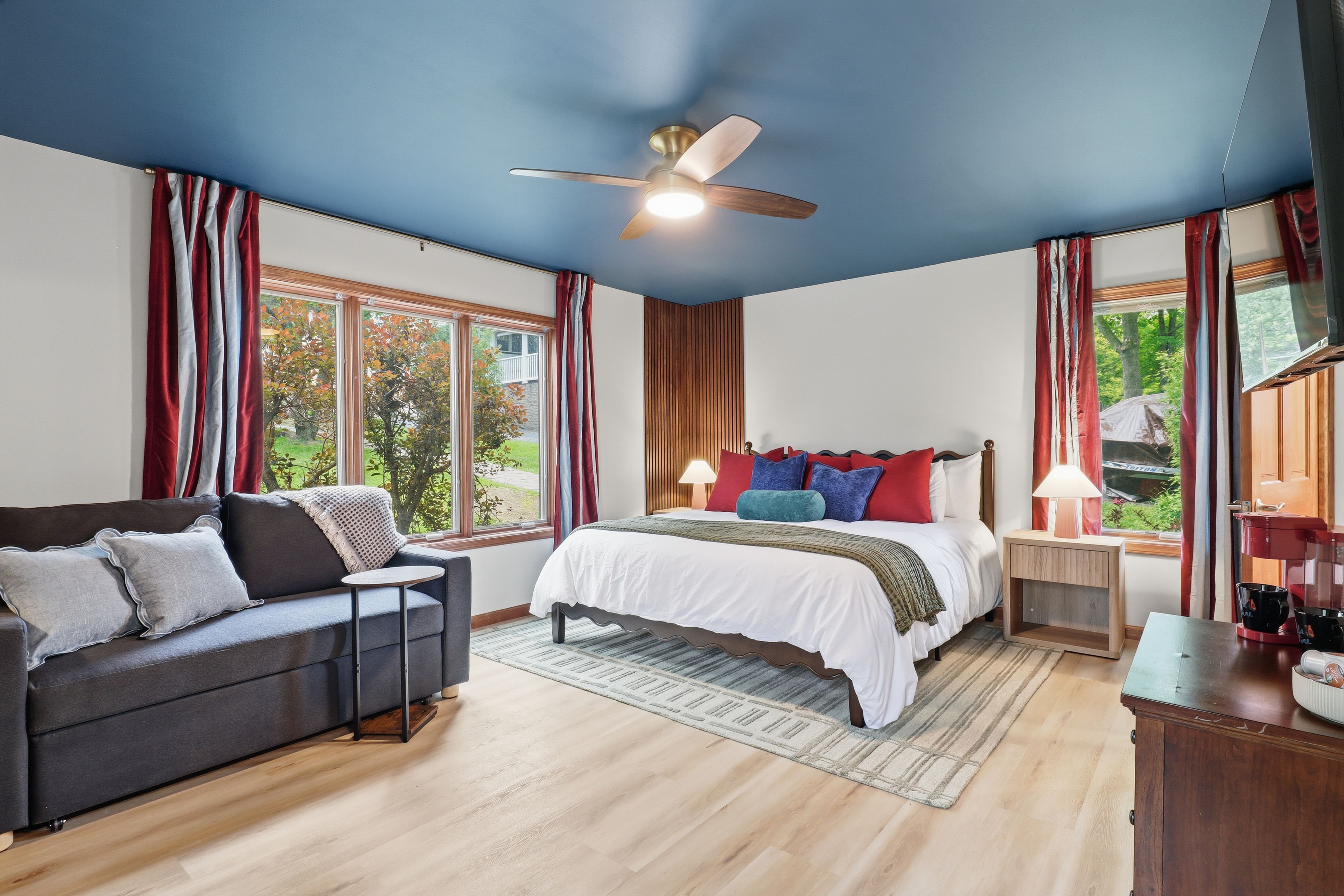 Ein Schlafzimmer mit Bett, einer Couch, einem Deckenventilator, einem Fenster mit Vorhängen und einer Kaffeemaschine.