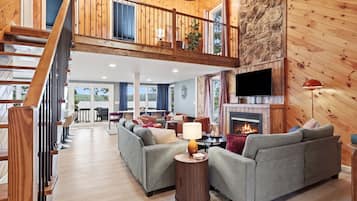 A spacious living area with a high ceiling, a fireplace, and a television.