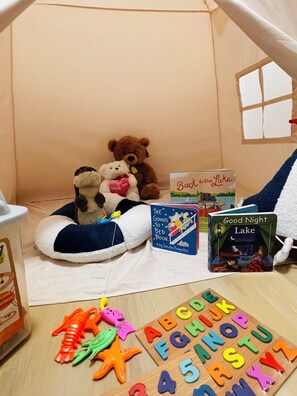 Un espacio interior acogedor para jugar, con una estructura parecida a una tienda de campaña, animales de peluche, libros infantiles y bloques del alfabeto.