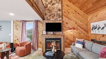 Ein modernes Wohnzimmer mit Kamin, Holzwänden, einer Couch, einem Fernseher und einer Treppe.