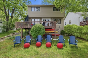 A two-story house with a deck, surrounded by greenery and outdoor seating.