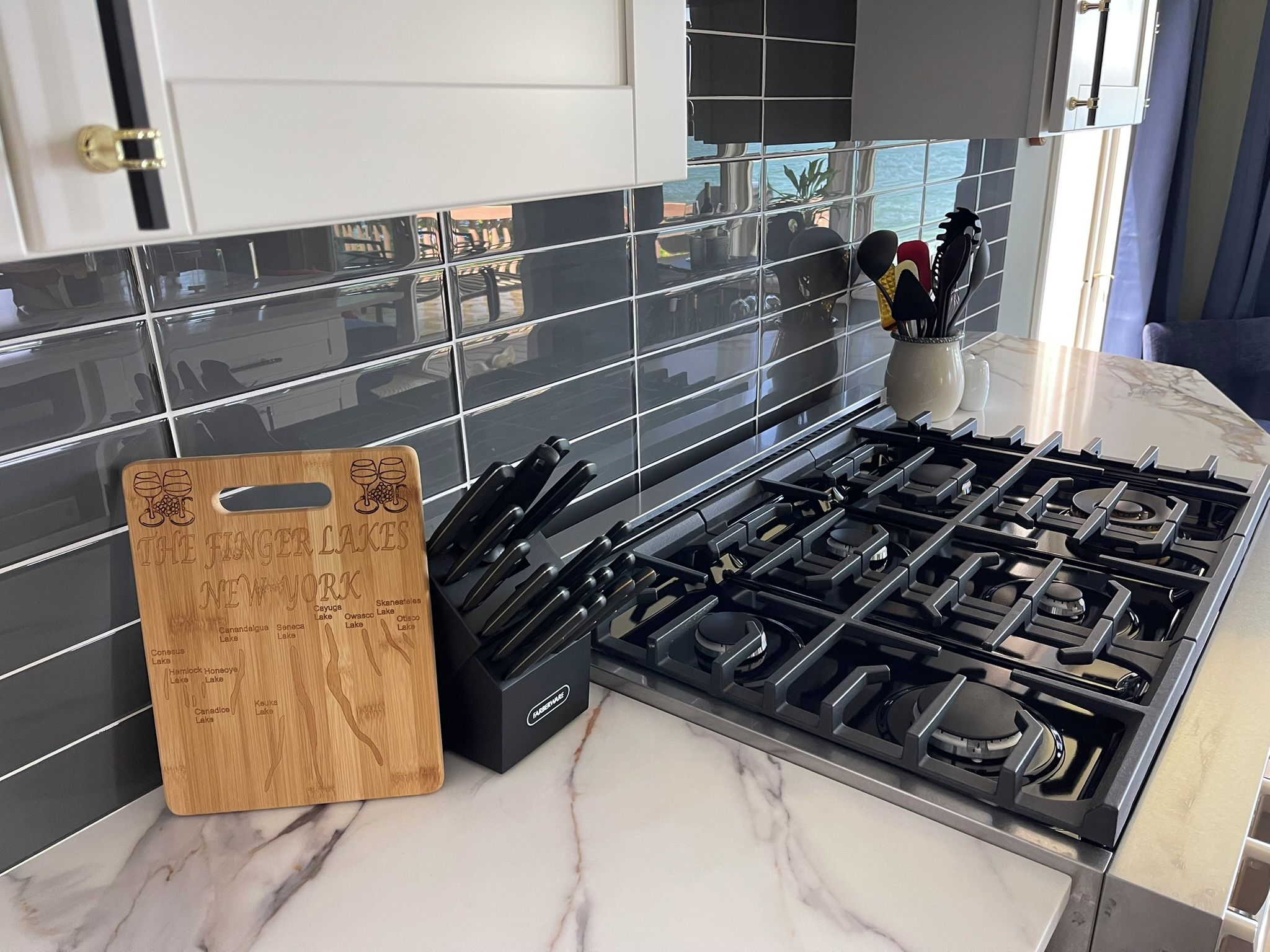 A kitchen with a gas stove, a wooden cutting board, and a tiled backsplash.