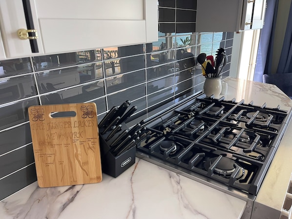 Una cocina con estufa a gas, tabla de cortar de madera y salpicadero de azulejos.