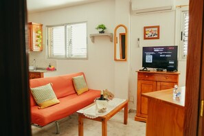 A living room with a sofa, a small table with a bottle, a TV on a wooden stand, and a window with blinds. - Apartment 2 | Aldea Blanca | 2 bedrooms | Hiking trails (Aldea Blanca)