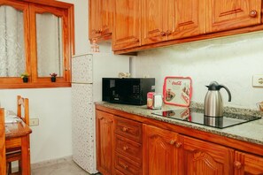 Eine Küche mit Holzschränken, einer Mikrowelle, einer Kaffeemaschine und einem Kühlschrank.