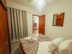 A bedroom with a bed, a wooden wardrobe, a mirror, and a door leading to another room. - Apartment 2 | Aldea Blanca | 2 bedrooms | Hiking trails (Aldea Blanca)