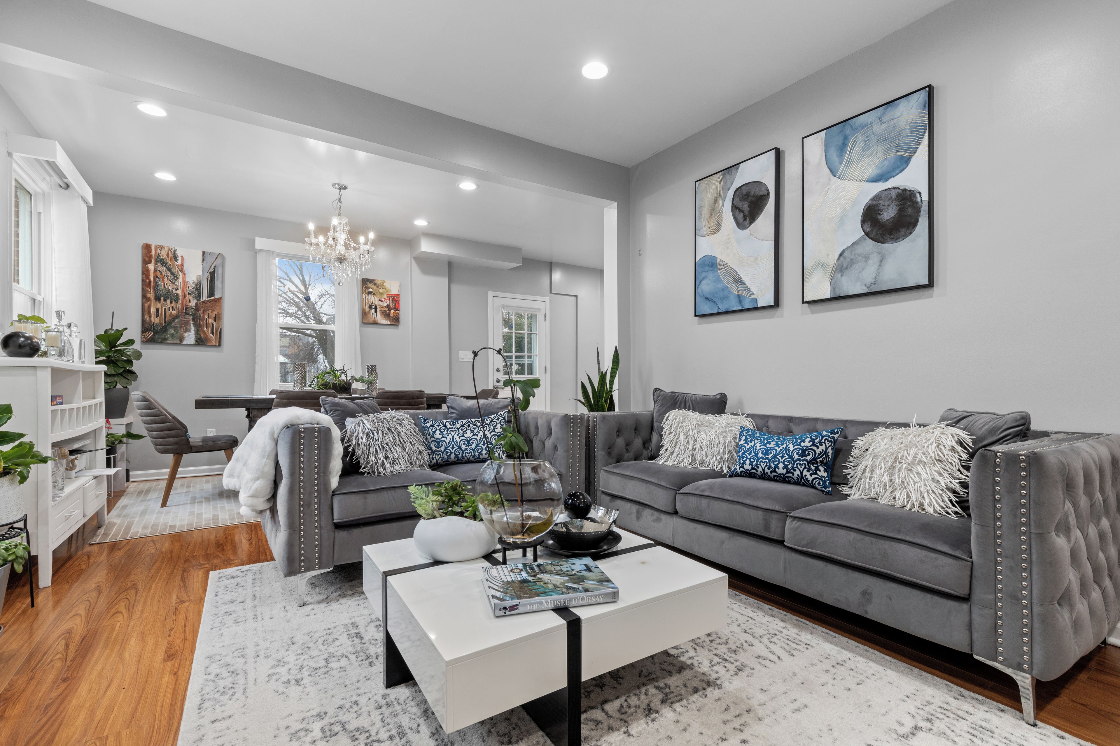 A modern living room with a grey sofa, a white coffee table, and a chandelier.