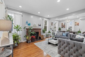 A spacious living room with a fireplace, a grey sofa set, and a chandelier.