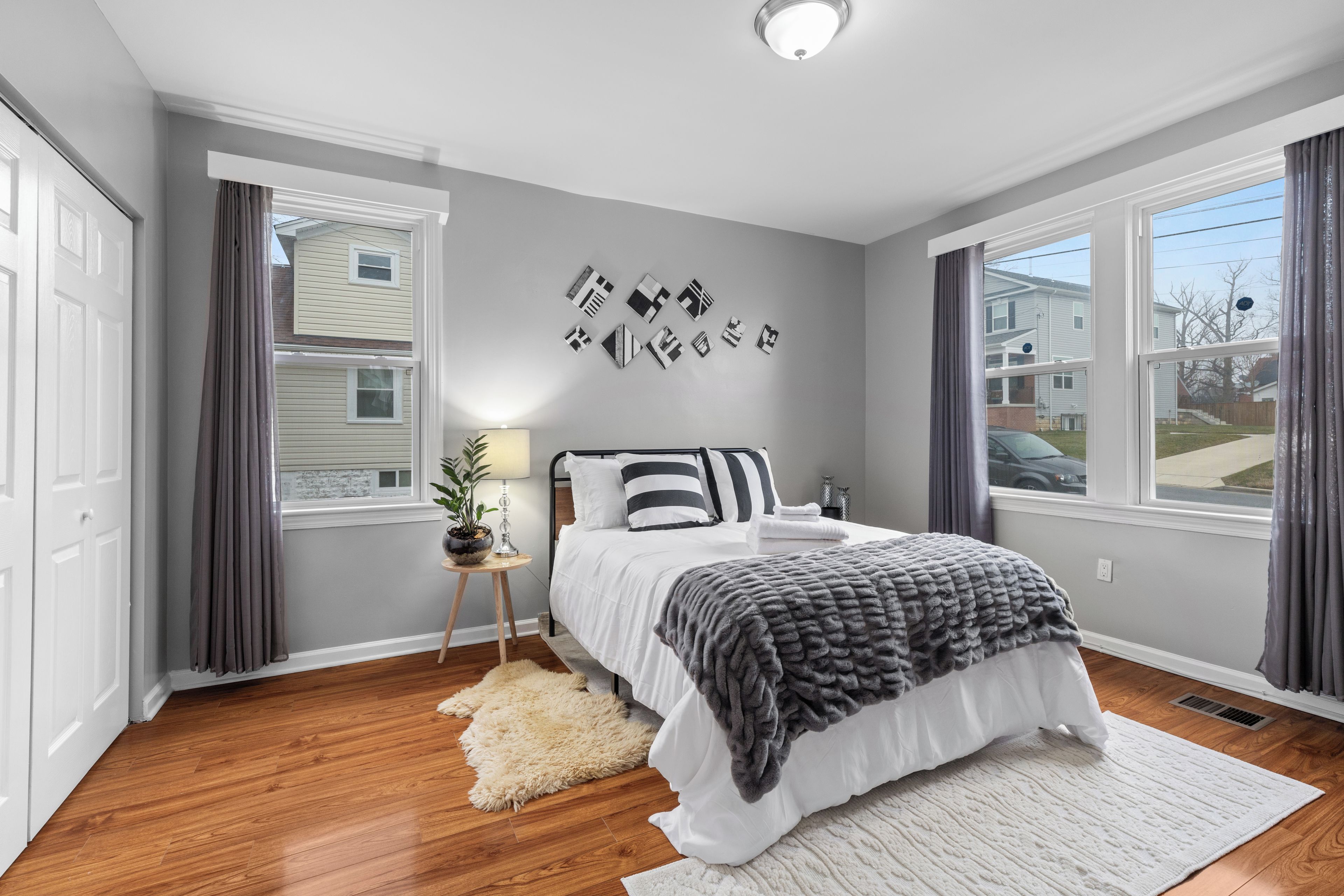 A bedroom with a bed, a nightstand, a lamp, a rug, and a wall with framed pictures.