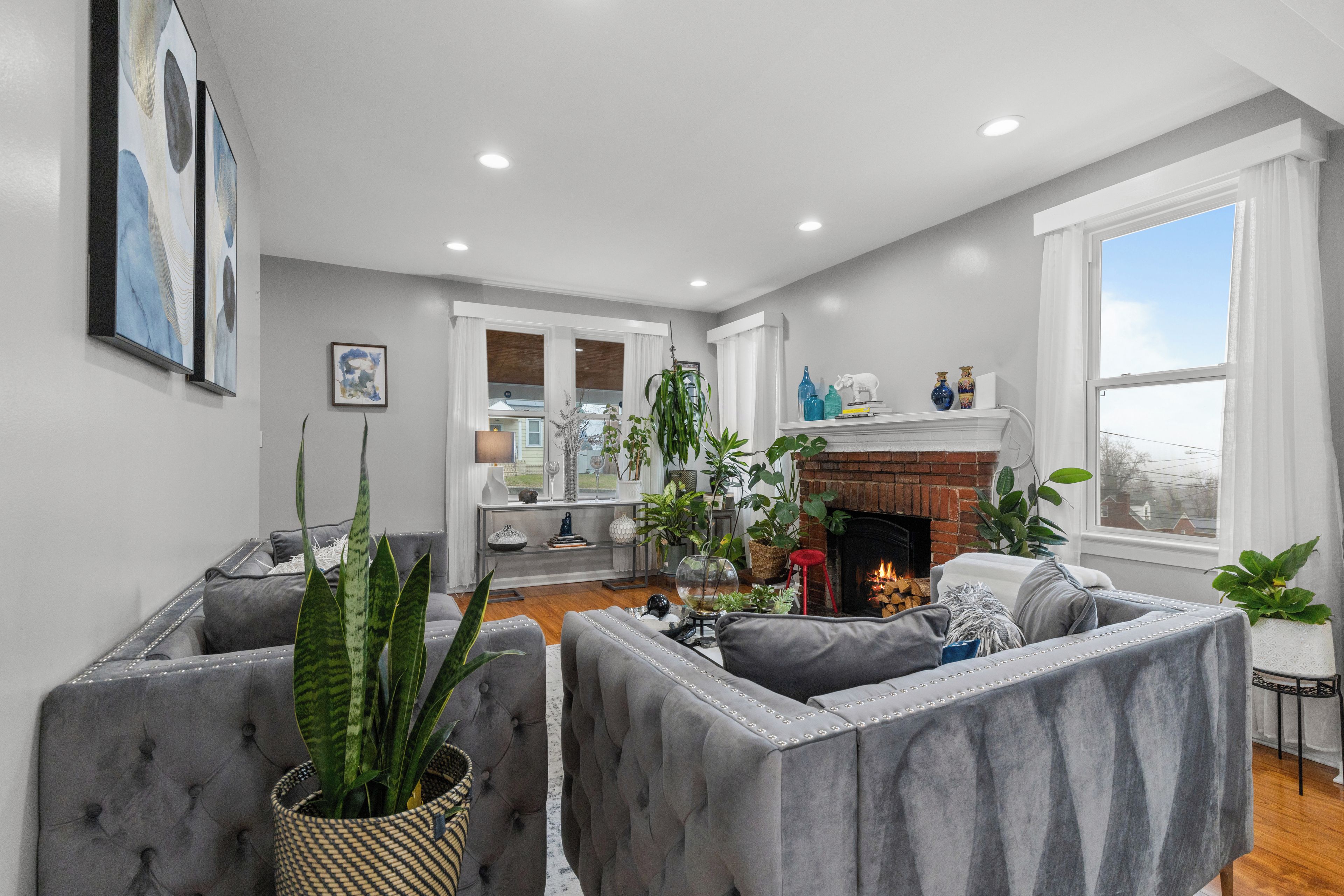 A living room with a fireplace, grey upholstered seating, and a large window.