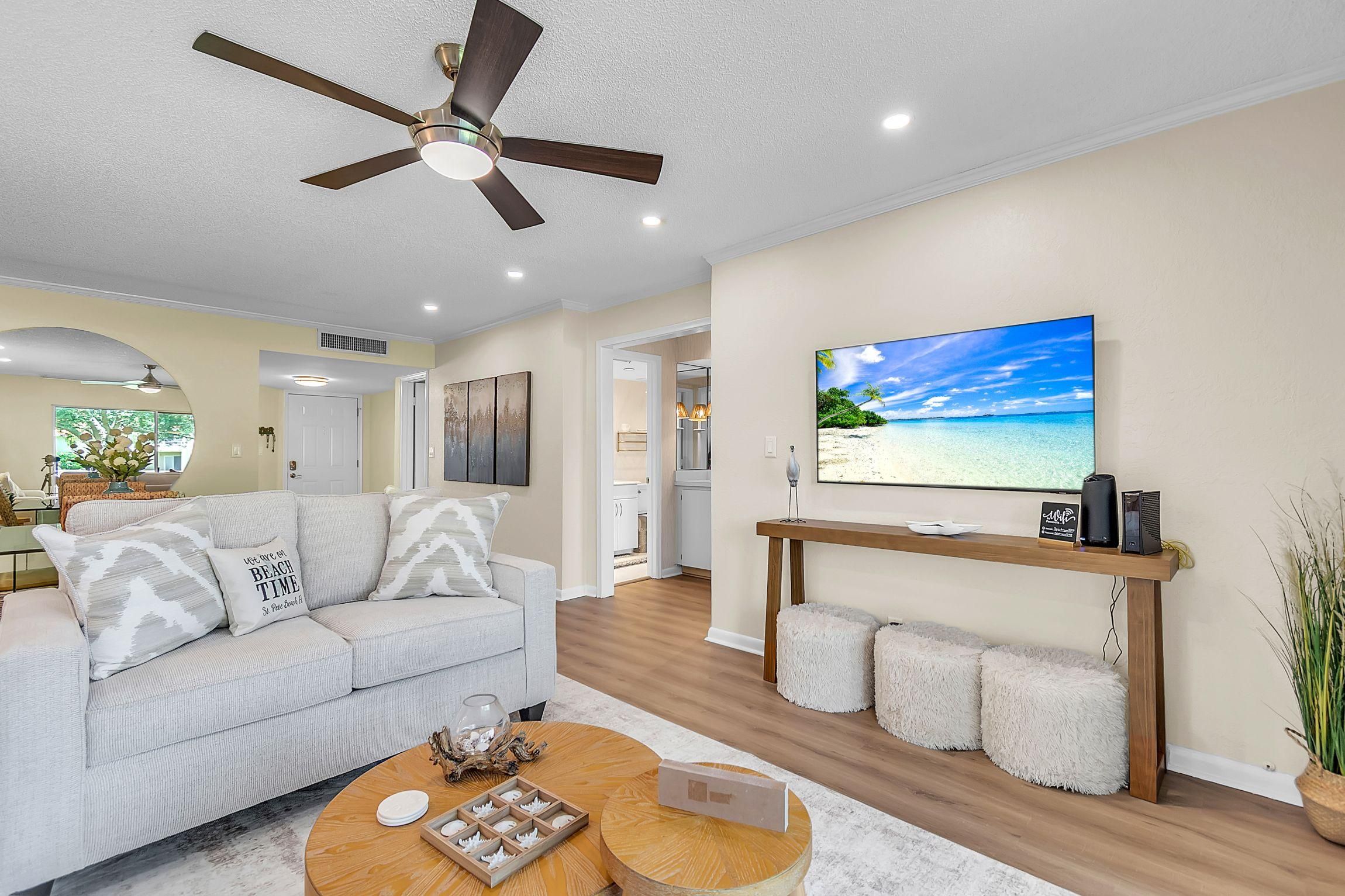 A modern living room with a ceiling fan, a large flat-screen TV, a sofa with decorative pillows, and a wooden coffee table.
