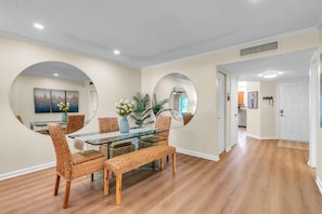 A dining area with a glass table, wicker chairs, and a large mirror on the wall. - Vista Verde East 105 (St. Petersburg)