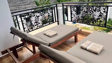 A balcony with two sun loungers, a decorative black metal railing, and a view of greenery and a building in the background.