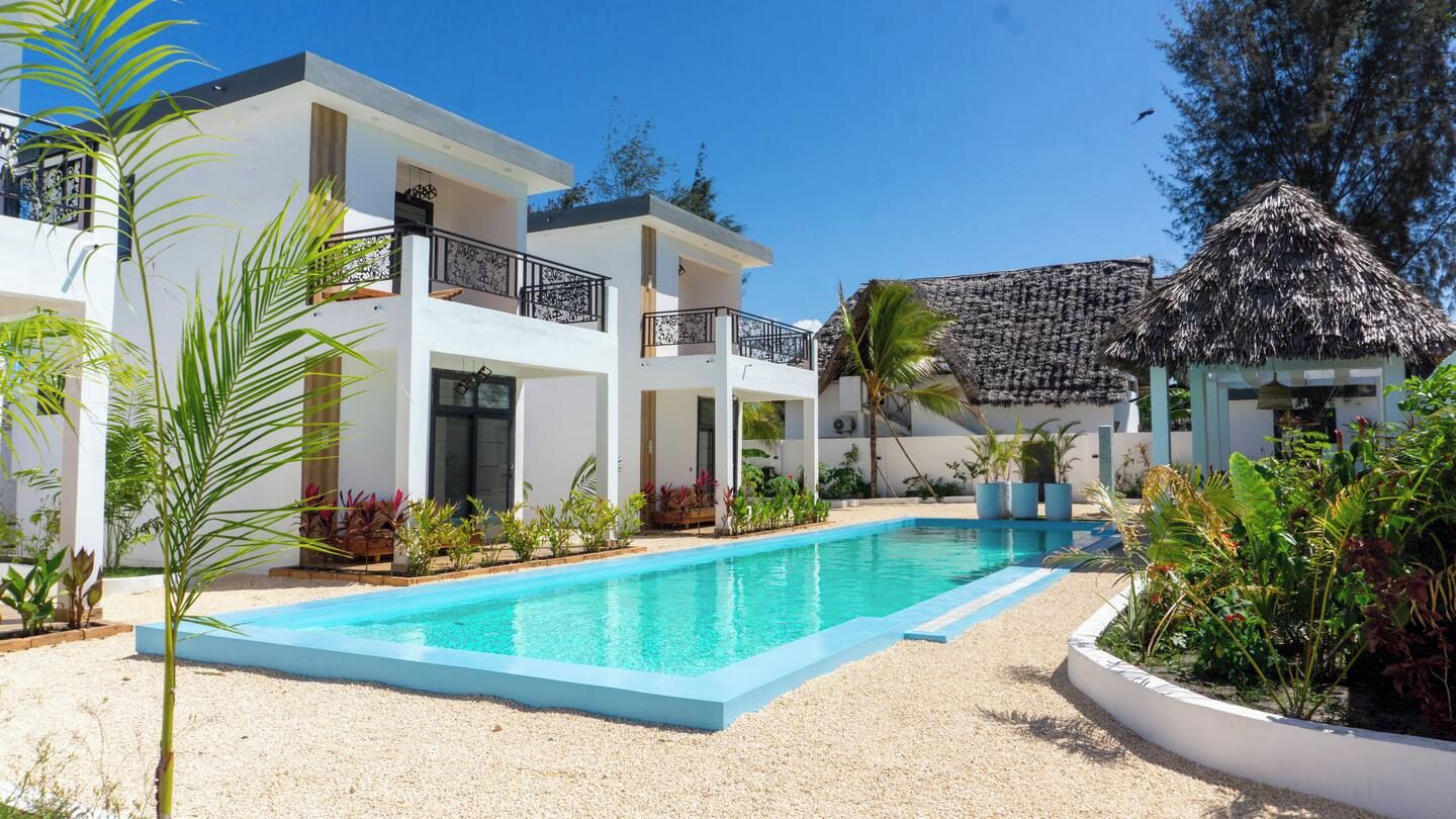 A modern hotel with a swimming pool, outdoor plants, and a thatched-roof structure.