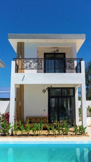 A modern two-story house with a balcony, a swimming pool, and a garden. - Kameleon Villa’s - Bungalow 2 (Kiwengwa)