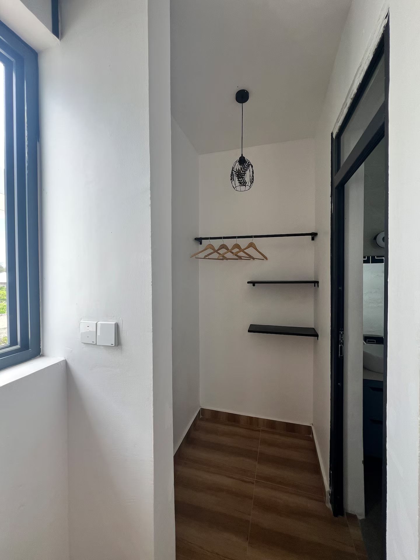 A hallway with a wooden floor, a hanging light fixture, and a coat rack with hangers.