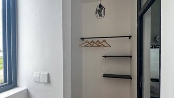 A hallway with a wooden floor, a hanging light fixture, and a coat rack with hangers.