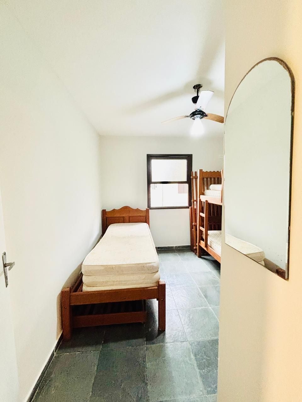 Una habitación pequeña con cama, ventana y ventilador de techo.