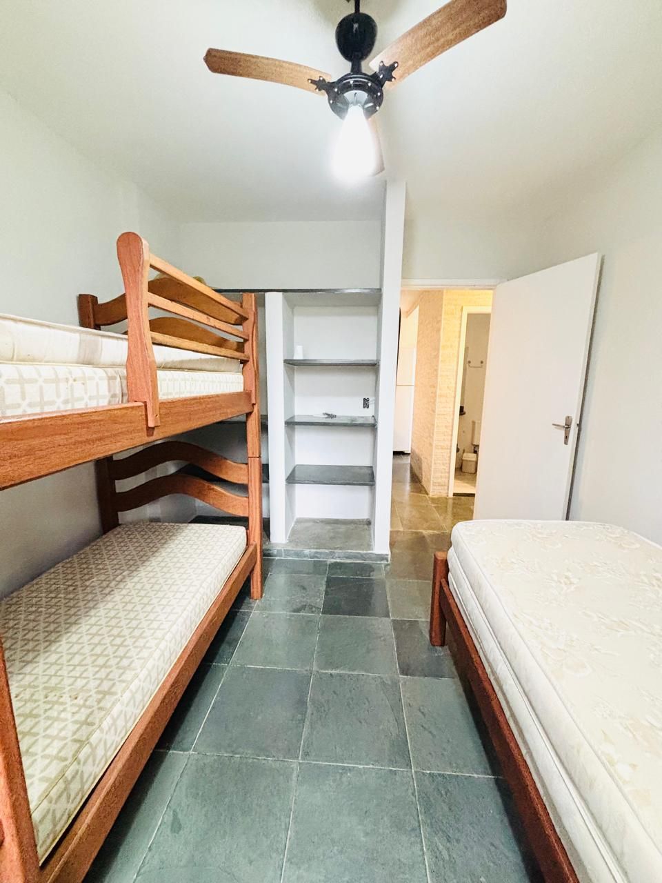 A room with bunk beds, a ceiling fan, and a staircase leading to a door.