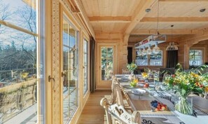 Een houten interieur met een eethoek, grote ramen en uitzicht op het omliggende landschap.