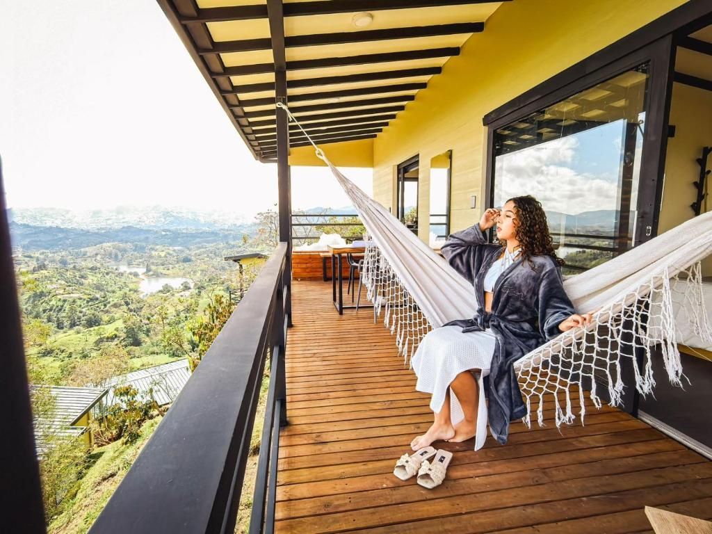 Una persona sentada en una hamaca en un balcón con vista a un valle.