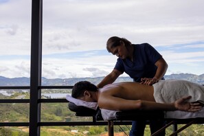 A massage therapy session in a room with a large window overlooking a mountainous landscape. - Alto Sereno (El Peñol)