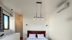 A modern hotel room with a large bed, a sitting area, and a view of the outdoors. - Kameleon Villa’s - Bungalow 3 (Kiwengwa)