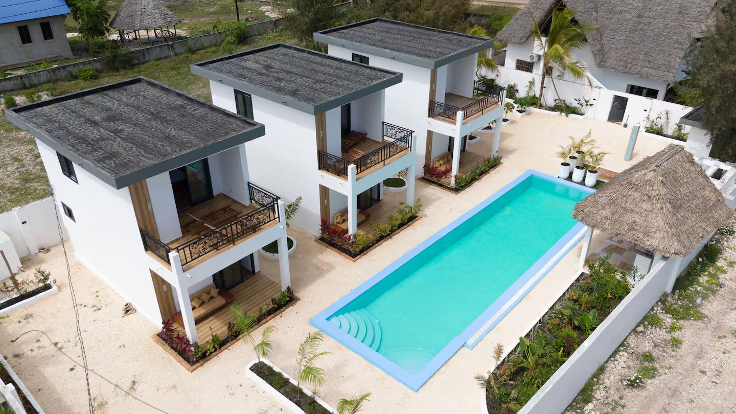 A modern resort with multiple two-story buildings, a central swimming pool, and thatched-roof structures.