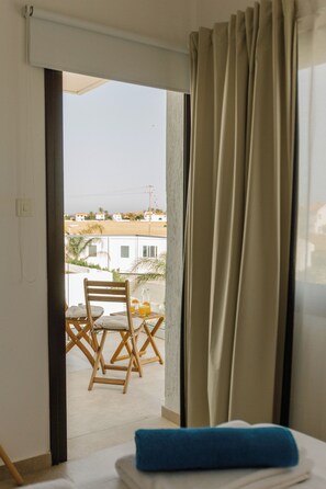 A room with a bed, a window with curtains, and a view of a balcony with a table and chairs. - Luxury Sea-View Villa with Private Pool & Coastal Charm in Larnaca. Book now! (Sophtadhes)