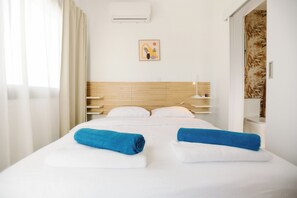 A hotel room with a bed, a headboard, a wall-mounted air conditioner, and a framed picture. - Luxury Sea-View Villa with Private Pool & Coastal Charm in Larnaca. Book now! (Sophtadhes)
