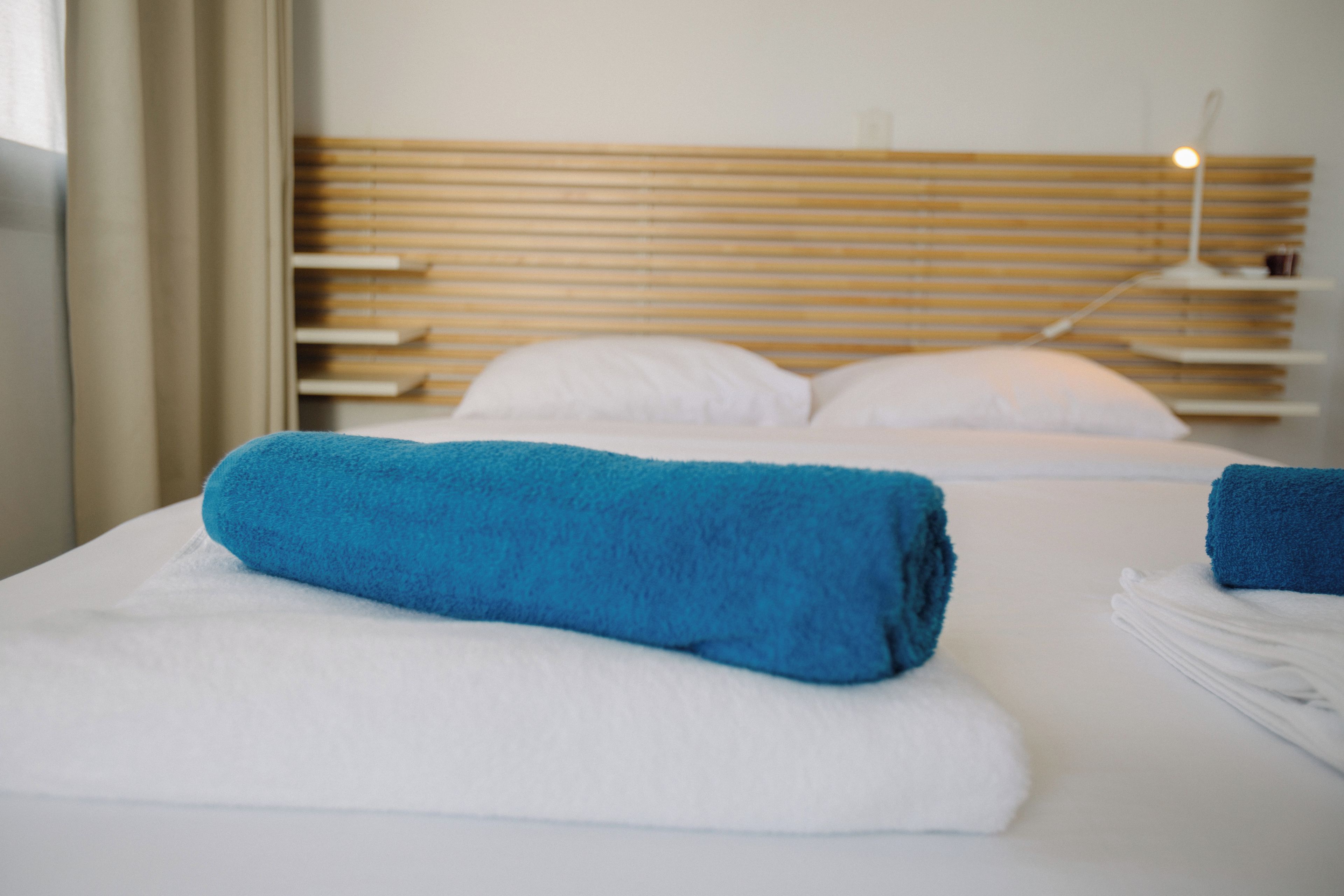 Une chambre d’hôtel avec un lit, du linge de lit blanc et une serviette bleue.
