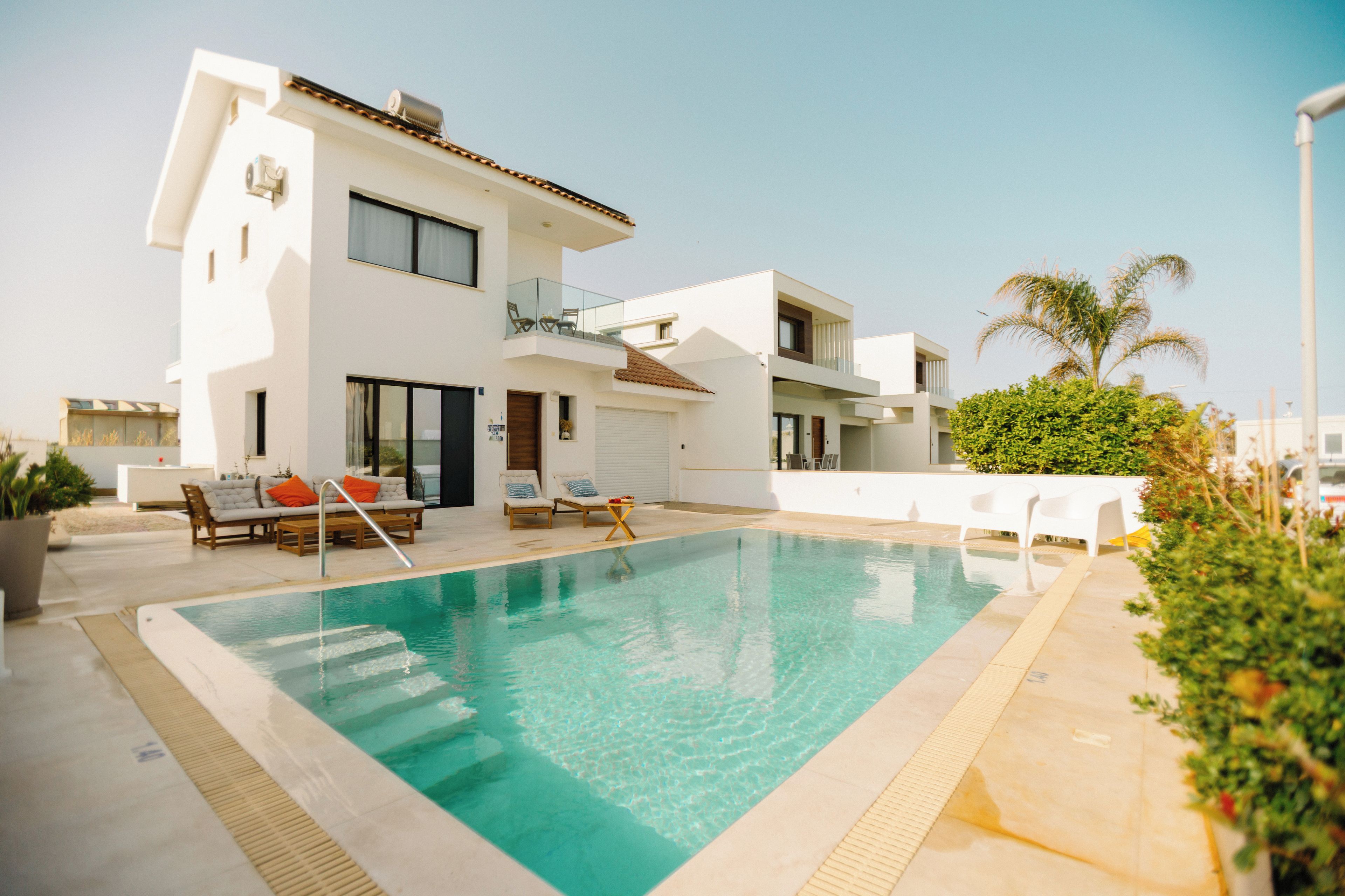 A modern two-story building with a swimming pool, outdoor seating, and a palm tree.