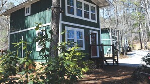 Une cabane à deux étages avec un porche, entourée d’arbres.