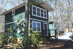 A two-story cabin with a porch, surrounded by trees. - Redesigned Mountain Cottage w/ Fireplace & Barn Wood Accents — Sleeps 4 (Lakemont)