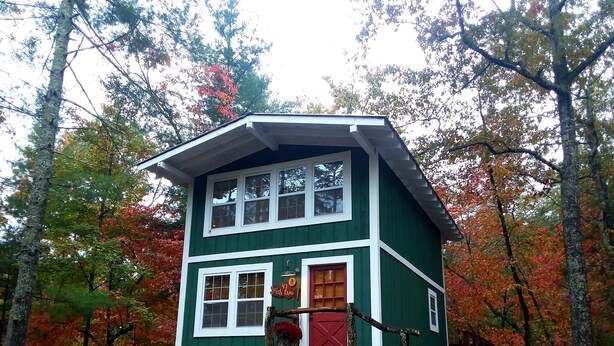 Une cabane à deux étages avec une porte rouge, entourée du feuillage automnal.