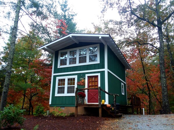 A two-story cabin with a red door, surrounded by autumn foliage. - Redesigned Mountain Cottage w/ Fireplace & Barn Wood Accents — Sleeps 4 (Lakemont)