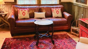 Un canapé en cuir marron agrémenté de coussins à motifs, une petite table ronde, un tapis rouge à motifs et une nichoir en bois posé sur un meuble rouge.