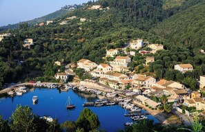 Un pueblo costero con un puerto deportivo, casas y un paisaje montañoso de fondo.