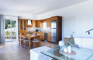 A modern kitchen with wooden cabinets, a dining area with a glass table, and a white sofa. - Evangelia, a tranquil Corfu retreat with panoramic sea views and easy village access (Kassiopi)