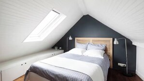 Une chambre avec un plafond en pente, un lit doté d’une tête de lit en bois, des lampes de chevet et une lucarne.