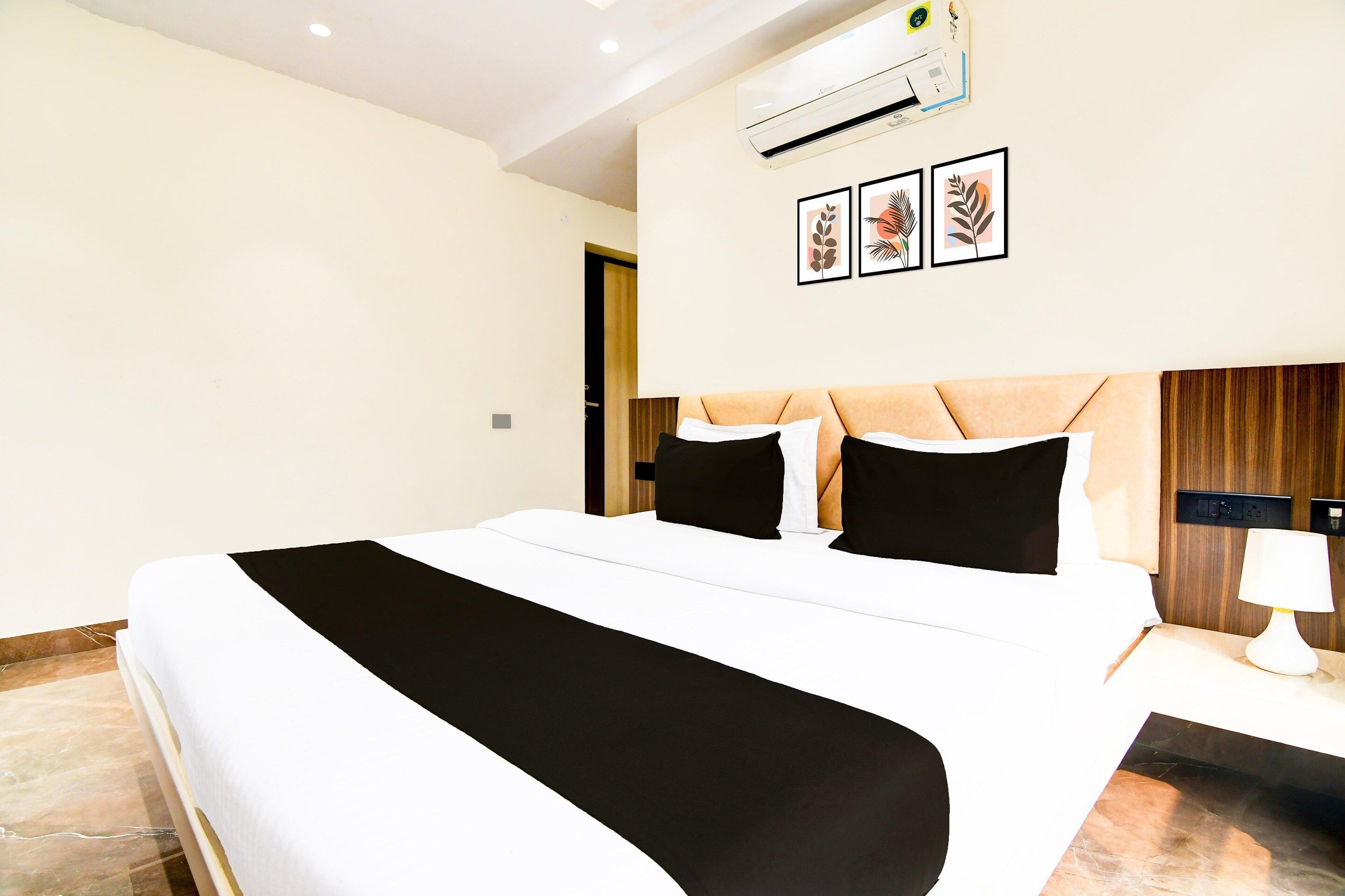 A hotel room with a large bed, a bedside table with a lamp, and a wall-mounted air conditioner.