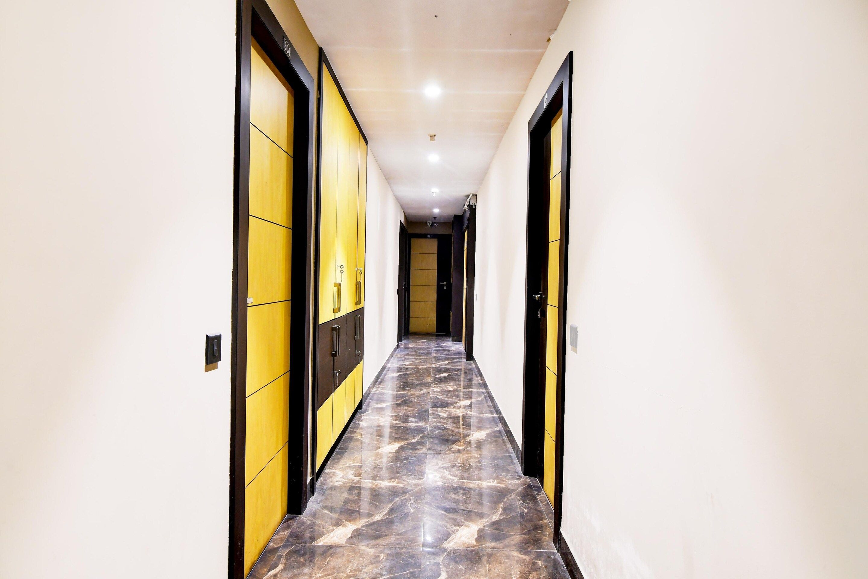 A hallway with a marble floor, yellow and black doors, and recessed lighting.
