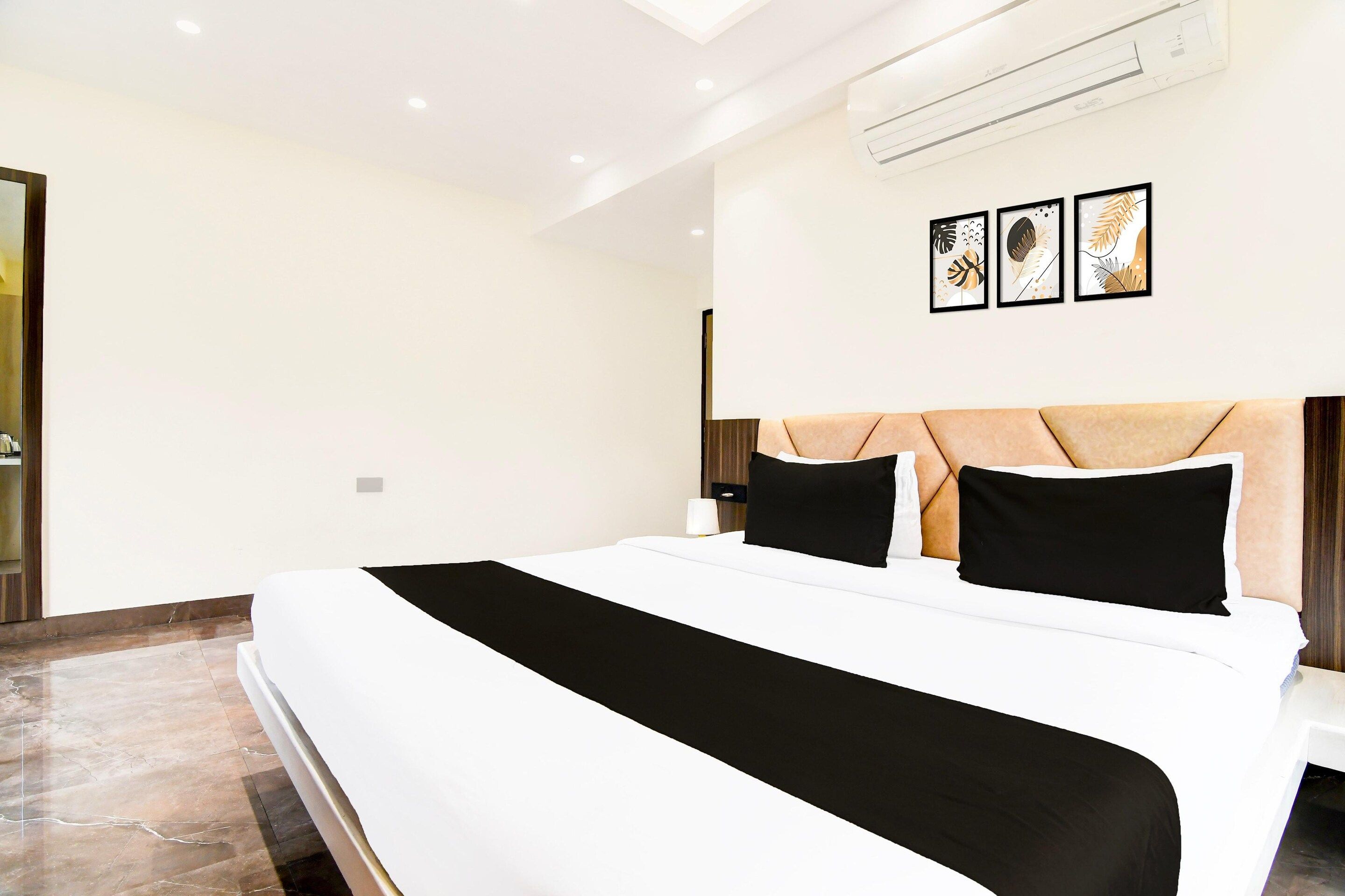 A modern hotel room with a large bed, a headboard with a geometric pattern, and three framed artworks on the wall.