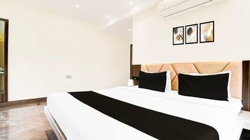 A modern hotel room with a large bed, a headboard with a geometric pattern, and three framed artworks on the wall.