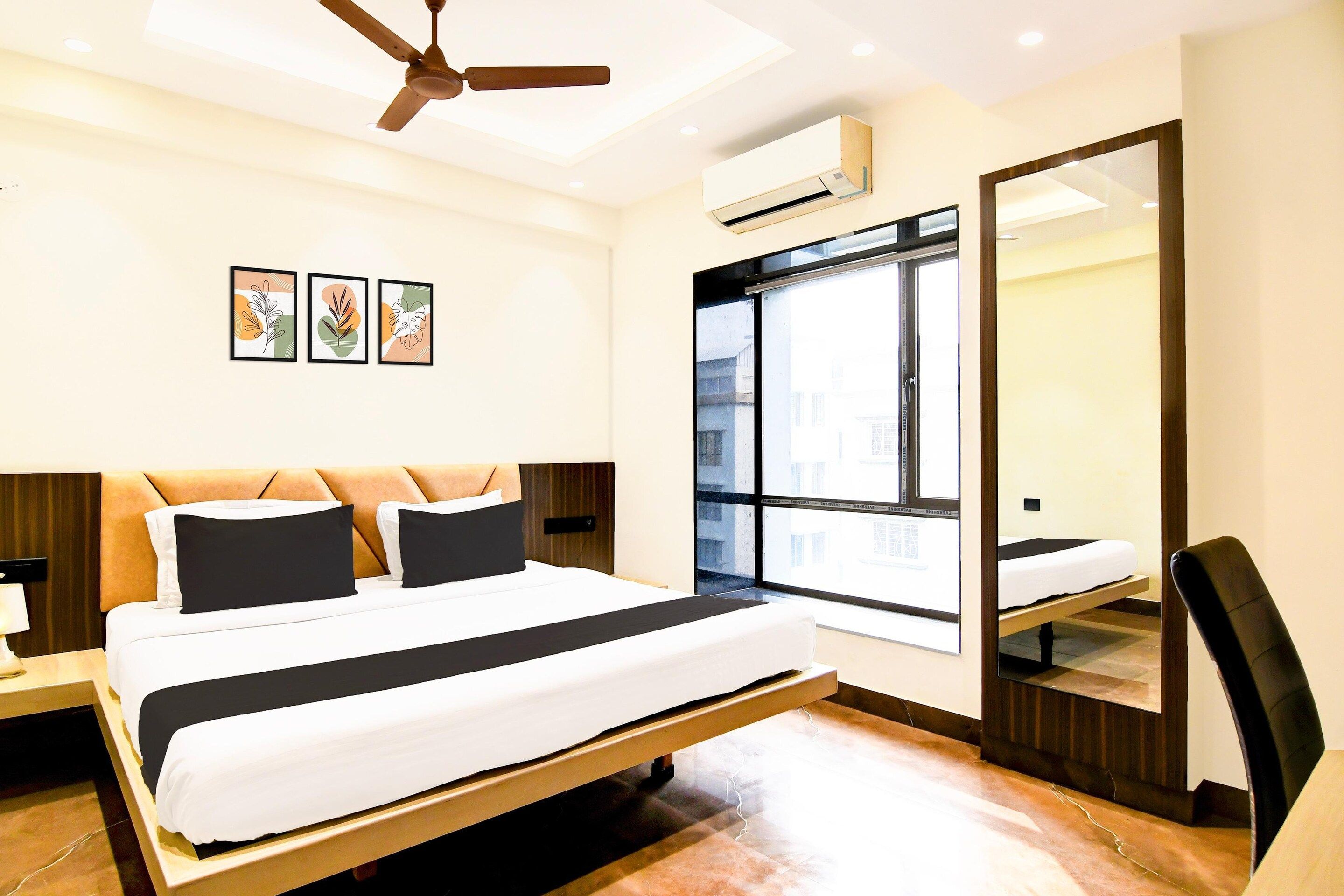 Una habitación de hotel moderna con una cama, ventilador de techo, equipo de aire acondicionado y un ventanal grande.