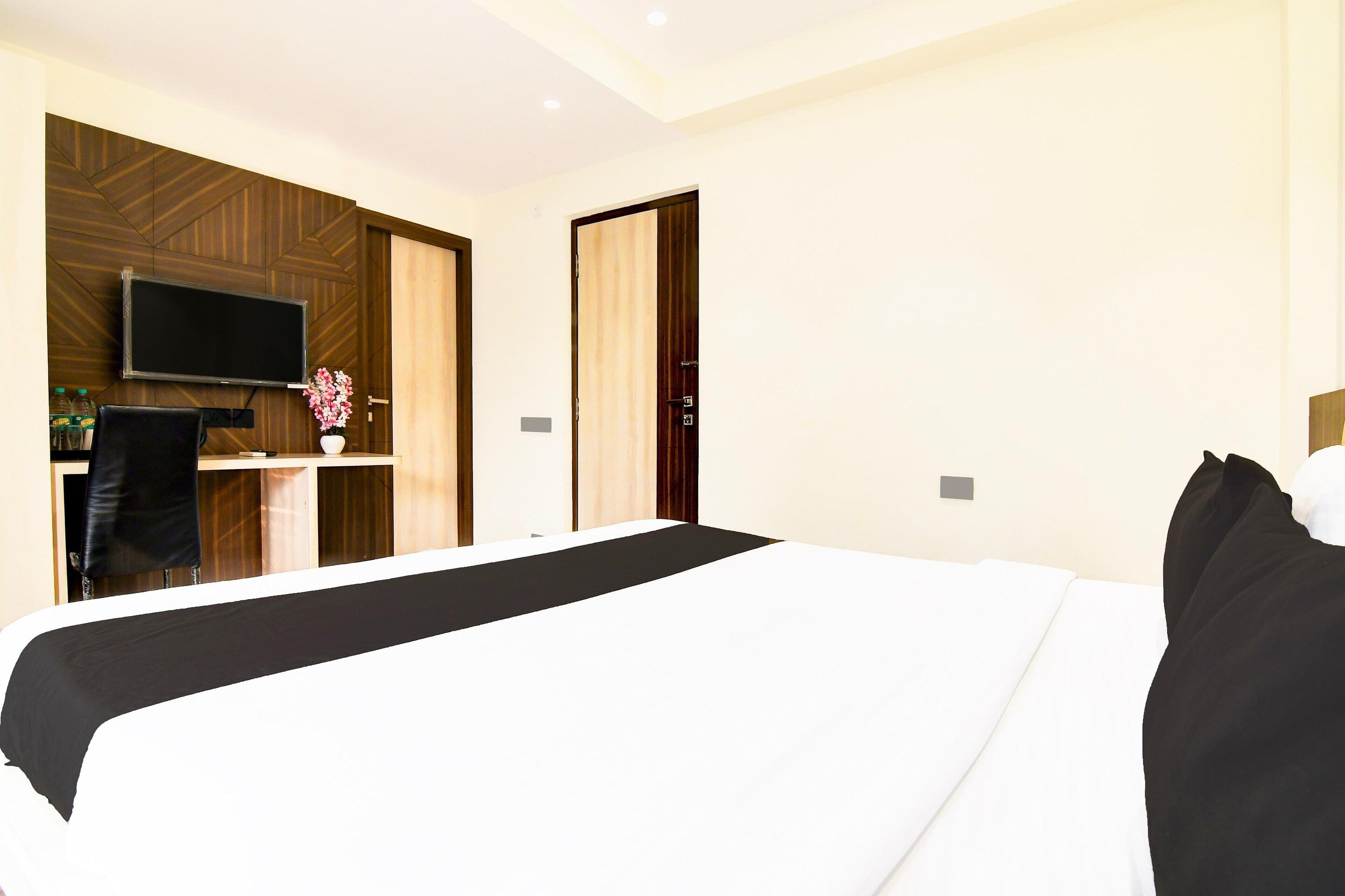 A hotel room with a large bed, a desk with a chair, a flat-screen TV, and a wooden accent wall.