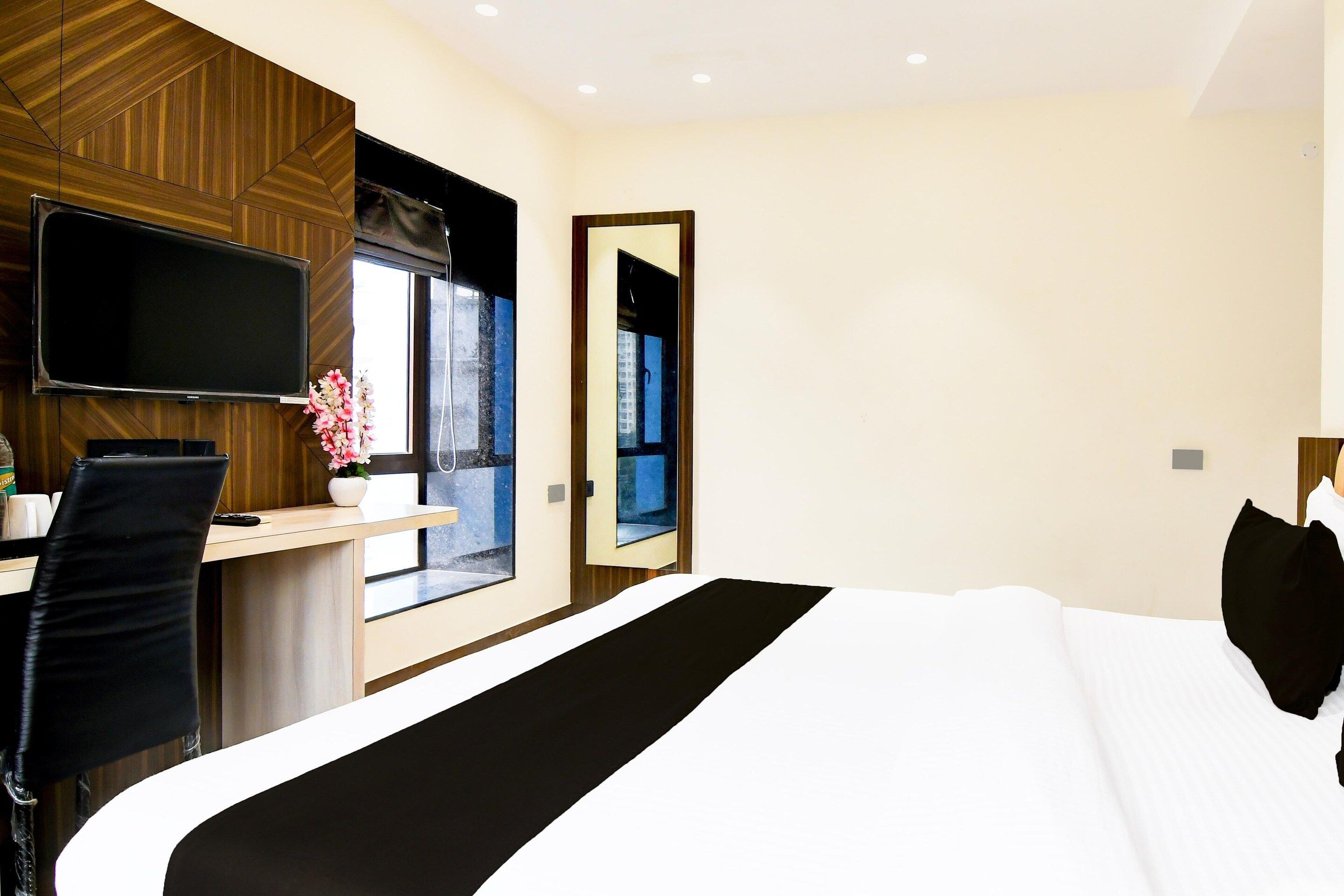 A hotel room with a bed, a desk with a chair, a TV mounted on the wall, and a window with a view.