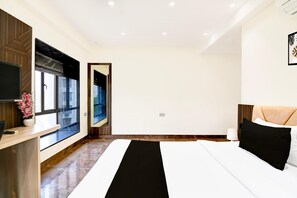 A modern hotel room with a large bed, a desk with a computer, a window with a view, and a mirror.