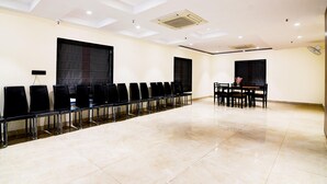 Un salón de conferencias con filas de sillas, una mesa con sillas y un ventanal grande.