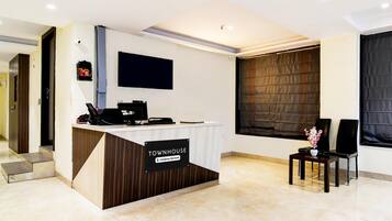 A reception desk with a sign reading "TOWNHOUSE Company Serviced." There are two chairs and a small table with a vase of flowers.